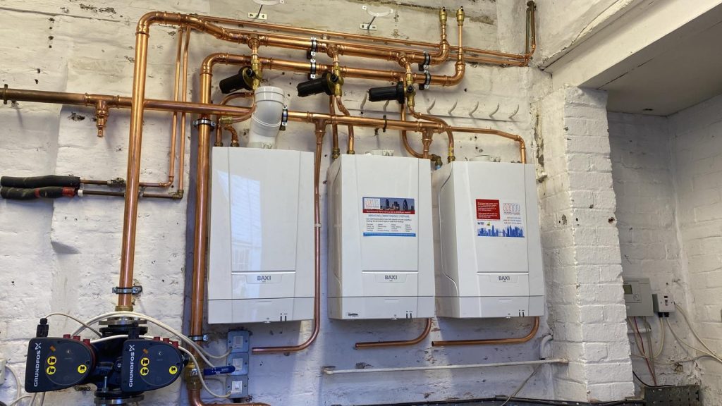 A plumbing setup showing three wall-mounted Baxi boilers connected by an extensive network of copper pipes.