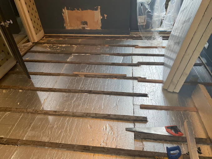 Partially installed underfloor heating system with silver insulation boards and wooden battens laid across the floor, with tools placed nearby during installation work.